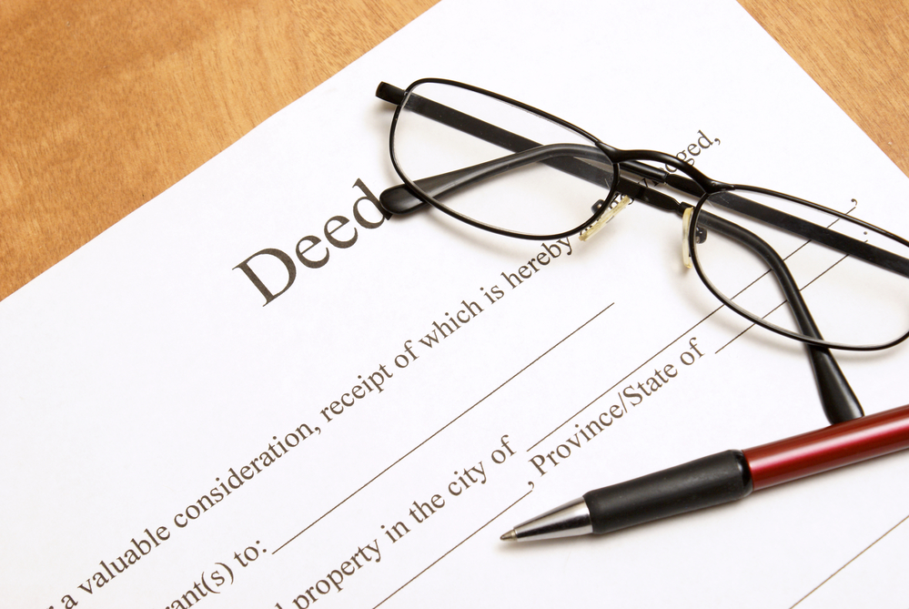 A closeup shot of deed papers and glasses to read the fine print.